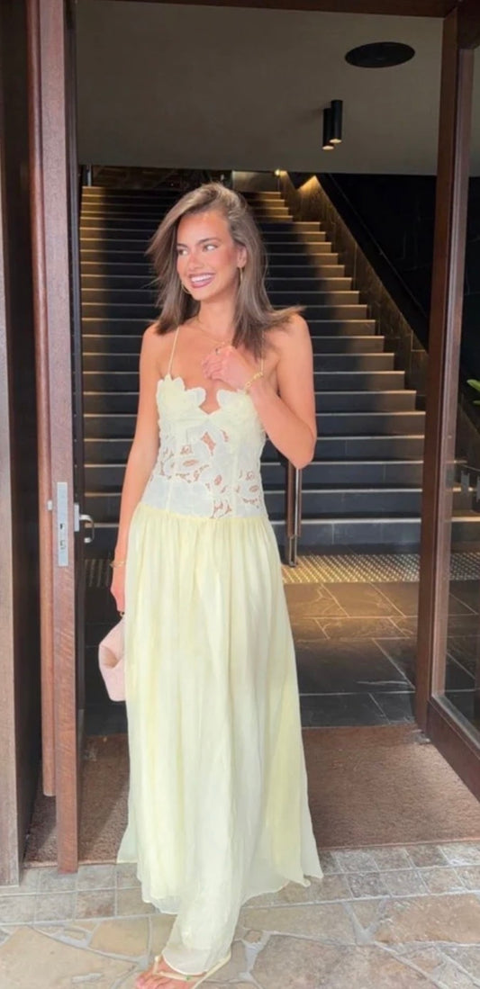 A woman wearing yellow Hansen and Gretel Stephanie maxi dress with a floral lace bodice stands in a doorway with a staircase behind her.