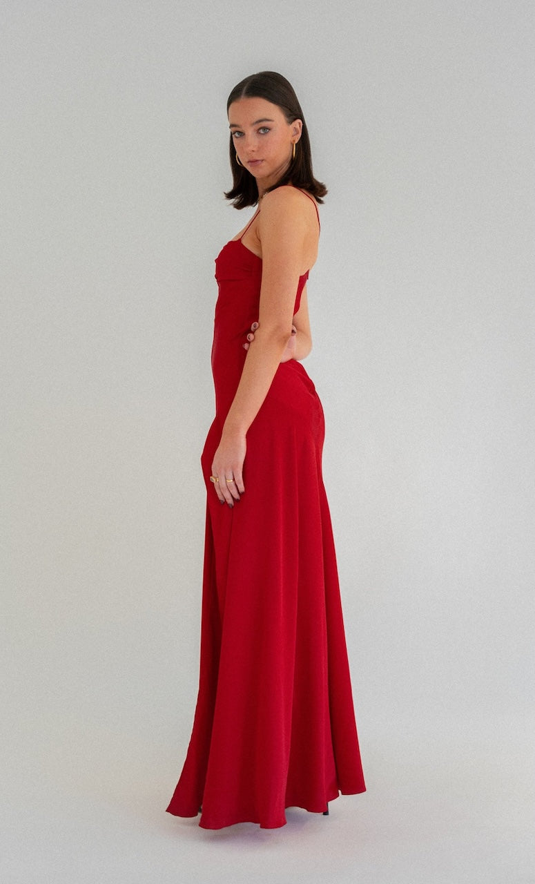 Hntr the Label Gaia Gown red showing side view of dress. Model with dark hair against a white background.