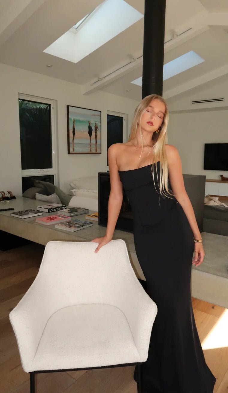 Hntr the Label Louie Gown Set Black Noir. Model stands holding white chair in black two piece dress with eyes closed.