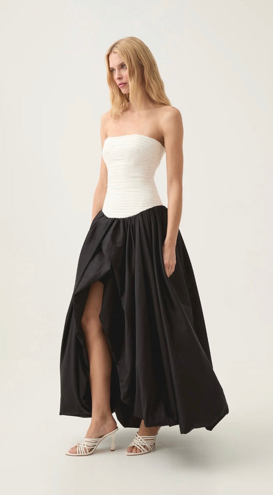 Aje Violette Bubble Hem Dress in Black and White. Model stands angled against a white background with white heels. 