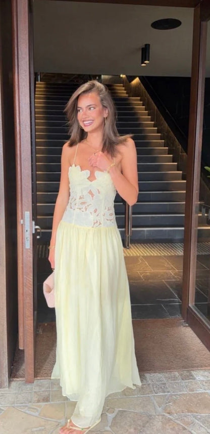 A woman wearing yellow Hansen and Gretel Stephanie maxi dress with a floral lace bodice stands in a doorway with a staircase behind her.