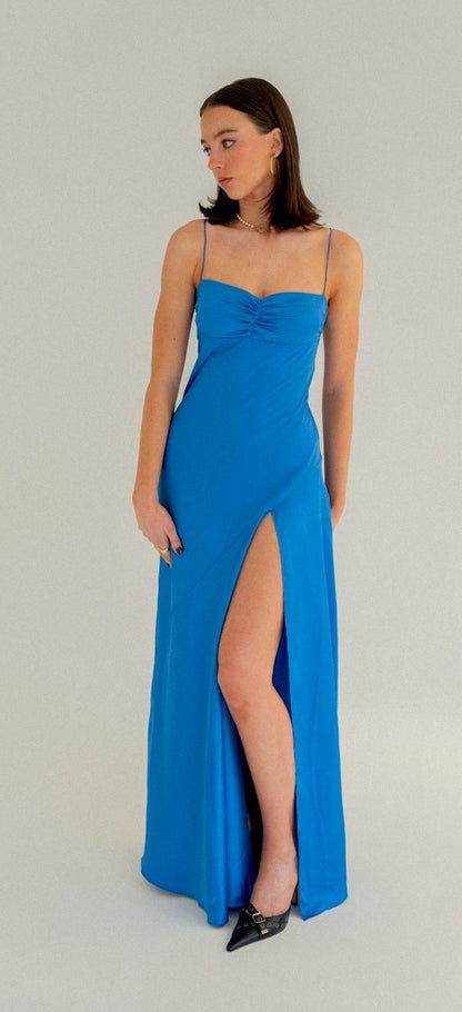Hntr Gaia Gown in Azul Blue. High leg split with ruched bust detailing. Model has dark hair and is against a white background. 