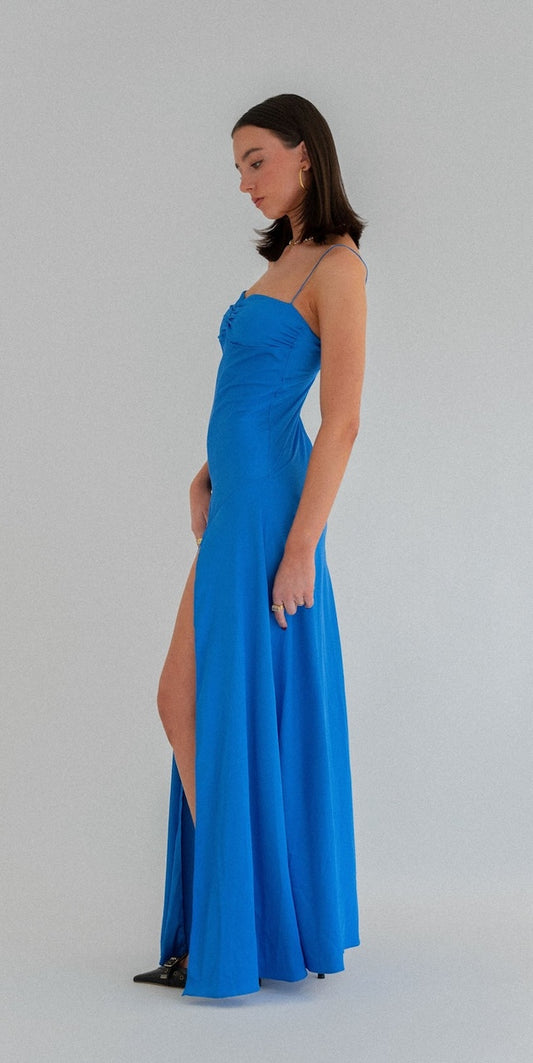 Hntr Gaia Gown in Azul blue. Side view of dress, model has dark hair and white background. 