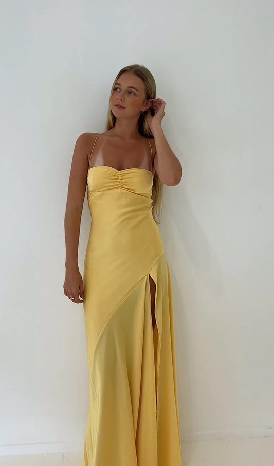 Hntr Gaia Gown Yellow Sun. Photo shows miodel with blonde hair against a white wall. The gaia Gown features a front split and ruched bust detailing. This dress went viral on TikTok 