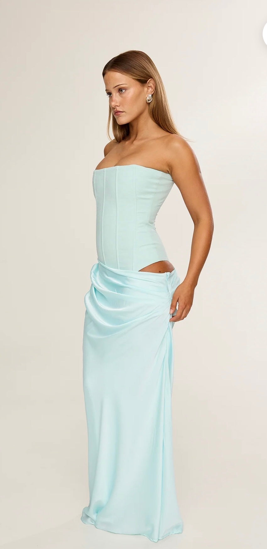Woman wearing a light blue strapless gown with sloping skirt waist band design on a plain background