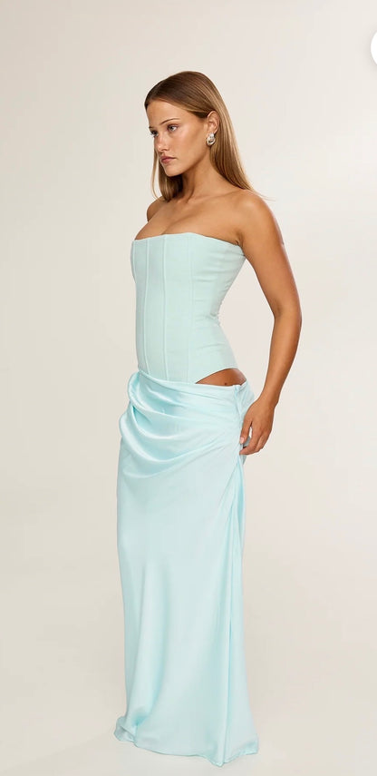 Woman wearing a light blue strapless gown with sloping skirt waist band design on a plain background