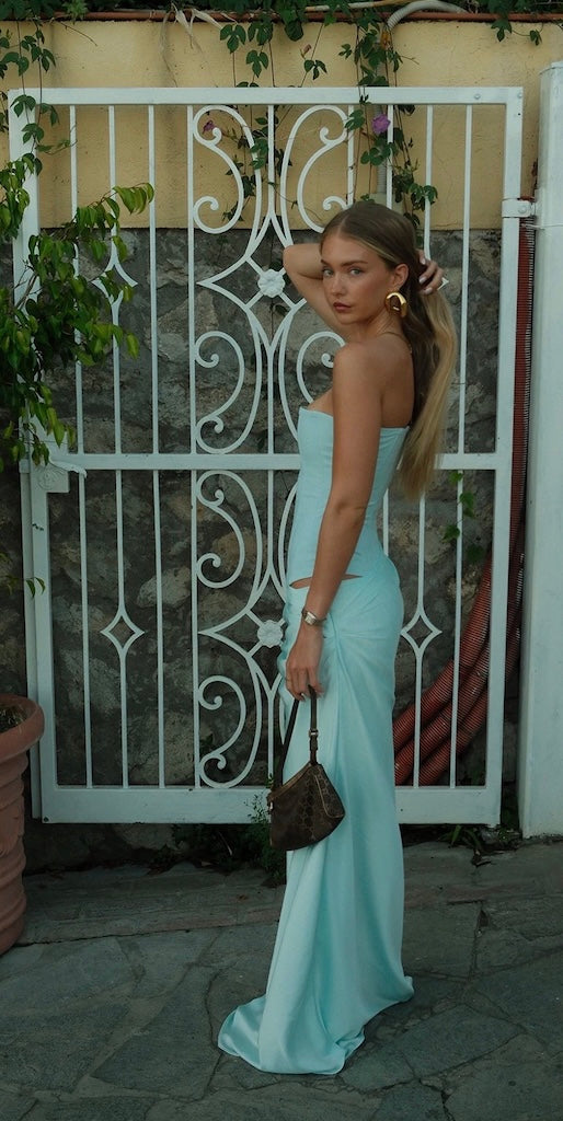 Woman in a light blue dress standing in front of an ornate white gate.
