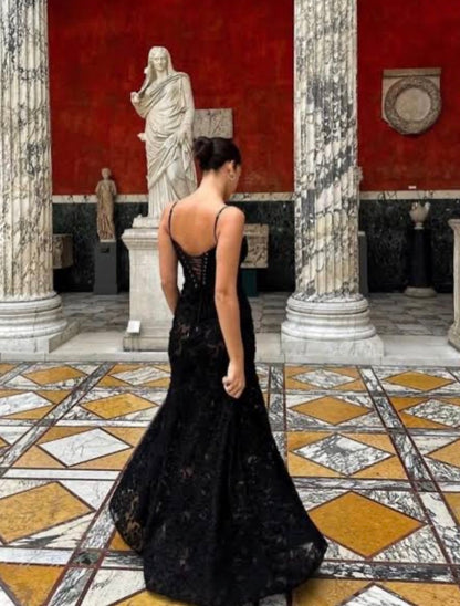 Woman in a black House of CB Seren dress standing in an elegant interior setting with classical columns and statues.