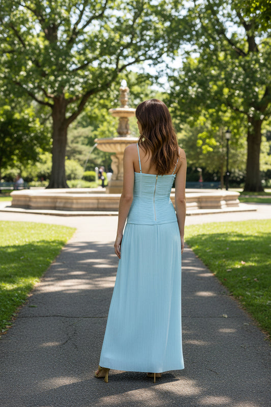 Model stands in public park with her back to the camera wearing a light blue Manning Cartell Gown. 
