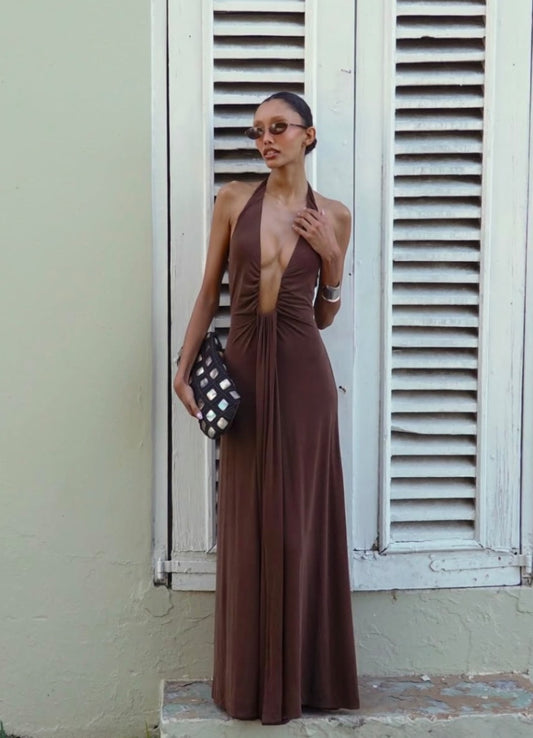 Woman in a brown halter neck Misha Jennifer Cupro dress standing in front of white shutters.