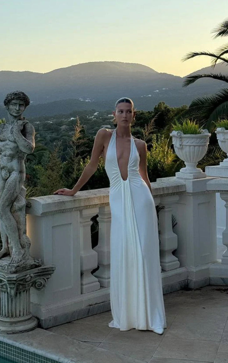 Woman in the Misha Jennifer Cupro white dress standing on a balcony with scenic background