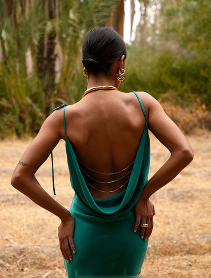 Woman in a Rat & Boa Ophelia green dress with an open back and gold chain detailing standing in a natural setting