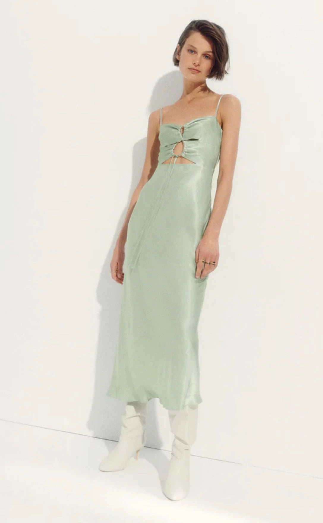 Shona Joy Felicity DRess in Thyme green full length view with model leaning against a white wall with white boots