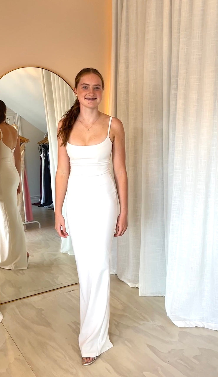 Nookie Bailey Gown in Ivory full length front view midel smiling in front of peach wall and arched mirror